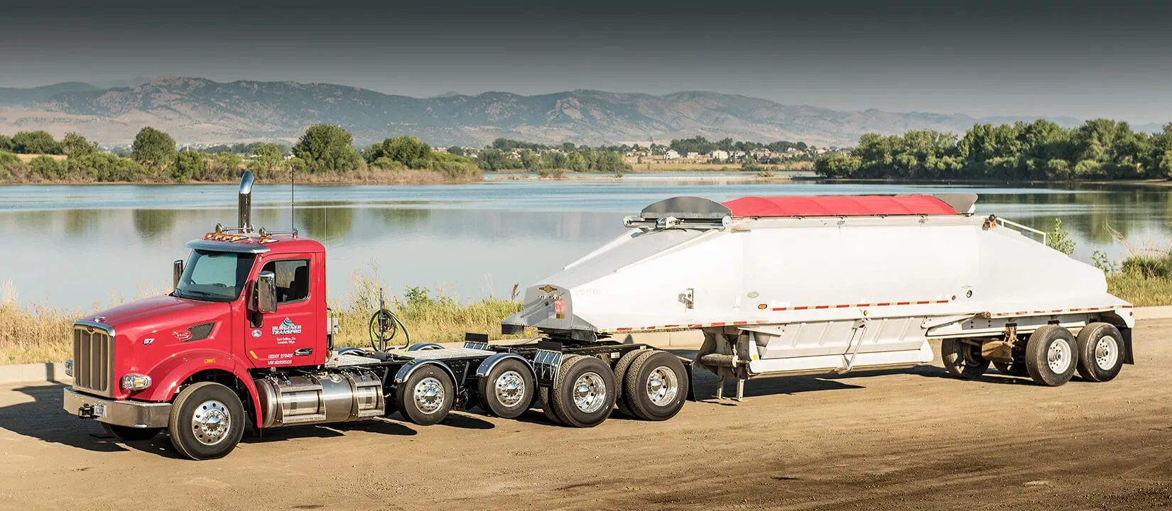TransPro truck and belly-dump trailer beside a lake with mountains